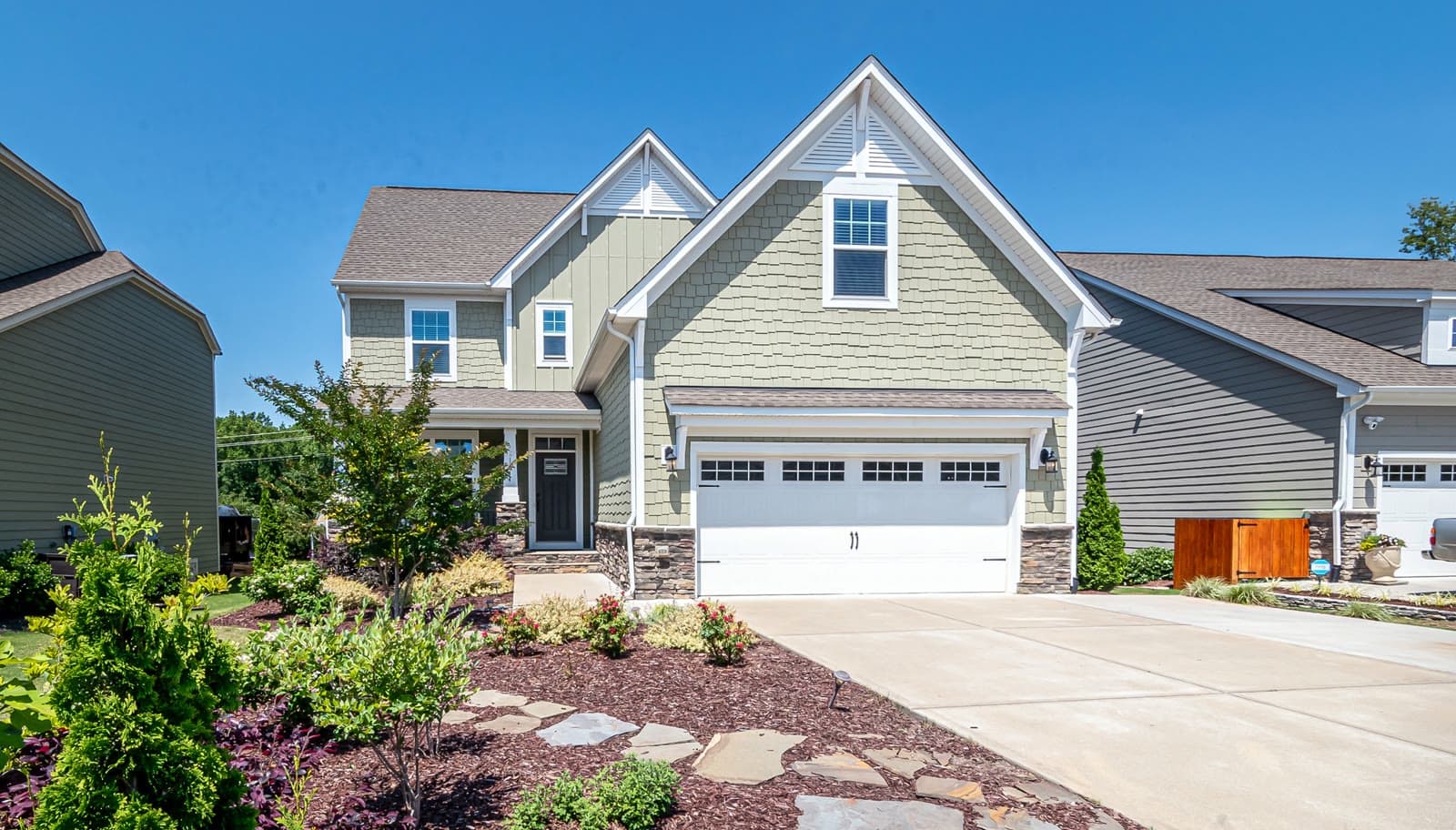 Modern farmhouse-style home with sage green siding, stone accents, and a beautifully landscaped yard, representative of the neighborhoods we serve